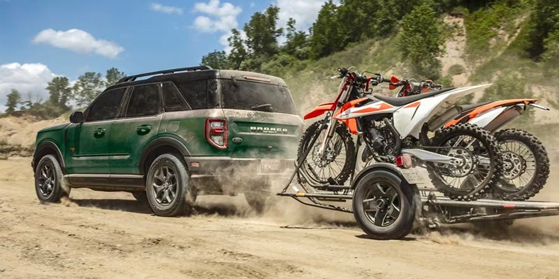 A green 2024 Ford Bronco Sport pulling a trailer with two dirt bikes secured down a dirt road