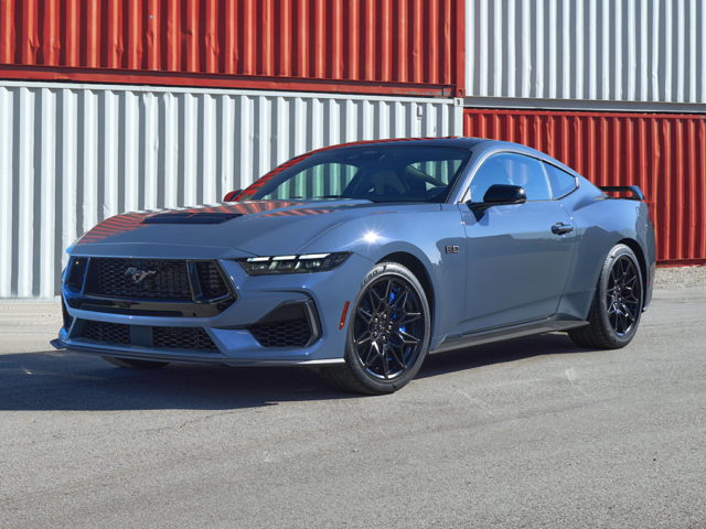 A blue 2204 Ford Mustang parked in front of a shipping container on a bright, sunny day