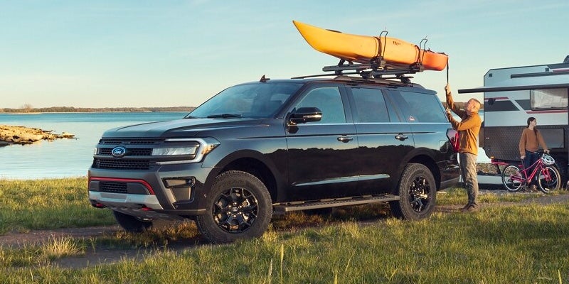 A black 2024 Ford Expedition parked near water with a yellow canoe secured to the roof rack on a sunny day