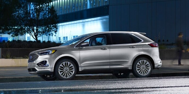 Silver 2024 Ford Edge driving down city street at night