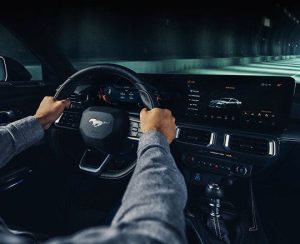 A person's hand on the steering wheel of a Ford Mustang. 