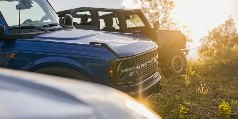 A view of the hoods of three 2024 Ford Broncos lined up next to another with the sun setting in the background