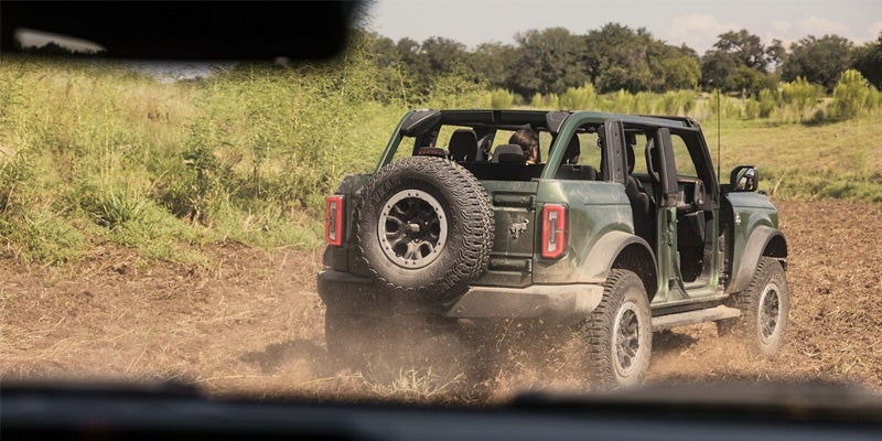 A green 2024 Ford Bronco driving through muddy water on a sunny day